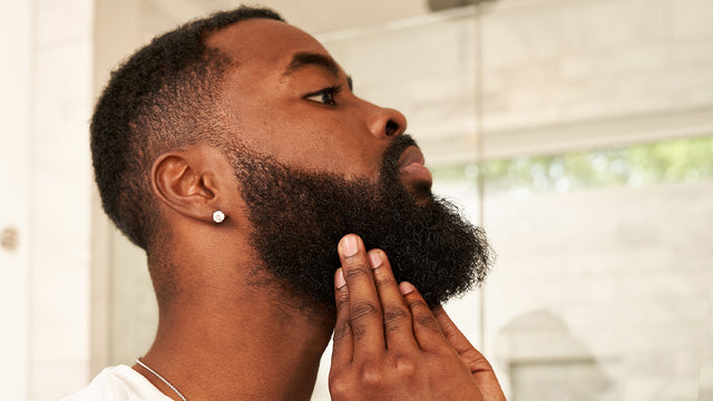 Profile of a handsome black man feeling his long beard. 
