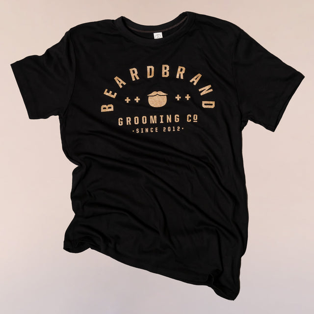 A faded black, “Dark Smoke” Beardbrand Banner Tee with gold ink print on the front.
