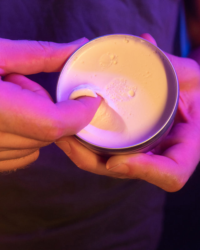 A person using their finger to scoop out some Beardbrand Styling Balm out of the canister with the lid open.