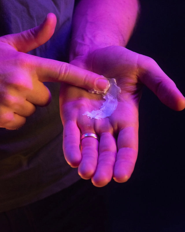 A finger spreading Beardbrand Styling Paste on a palm to show its consistency under purple lighting.