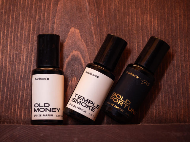 Beardbrand cologne collection featuring Old Money, Temple Smoke, and Bold Fortune eau de parfum bottles arranged on wooden background.