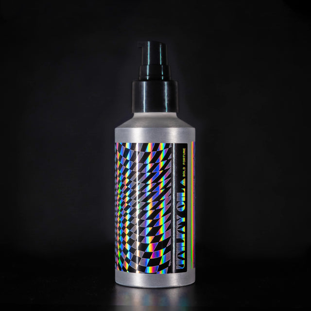 A bottle of Beardbrand Bold Fortune Utility Oil with a holographic label and black geometric 'tumbling blocks' pattern design.