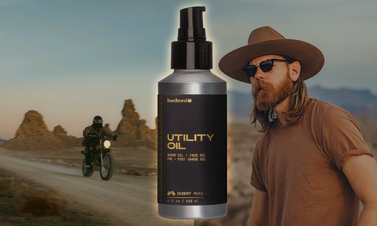 Beardbrand Utility Oil Desert Road scent in black pump bottle, featuring bearded man in brown hat and sunglasses with desert motorcycle scene background.