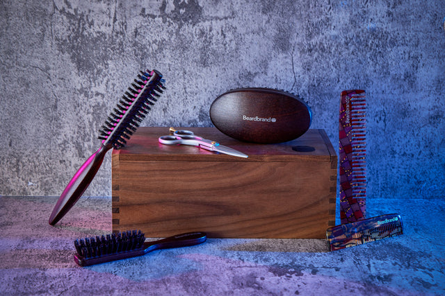 Grooming tools on and around a wooden box against a textured wall, including brushes, scissors, and combs.