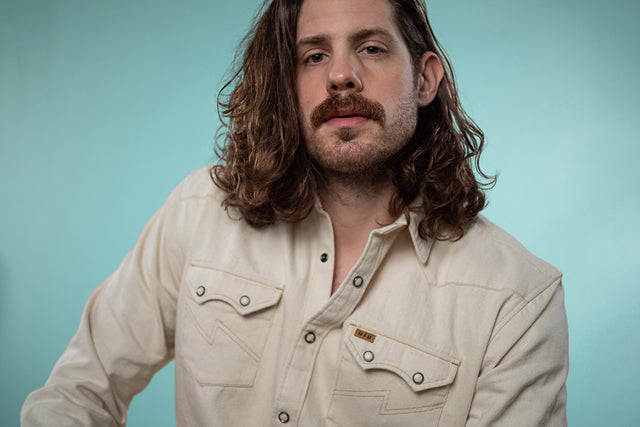 A portrait of Mike against a light teal backdrop wearing a pearl snap shirt.