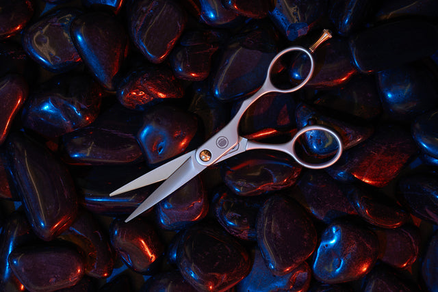 Beardbrand Trimming Scissors with the blades slightly open on shiny black stones with neon red and blue lighting accents.