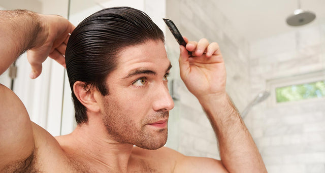 Handsome man standing in the bathroom, combing his freshly washed brown hair. 