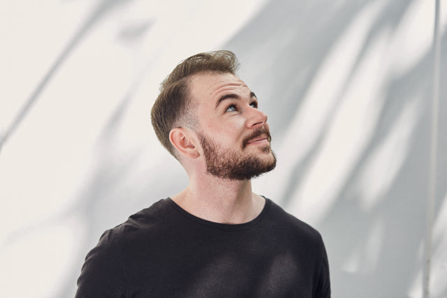 Handsome man with a short brown beard and a neatly trimmed neckline is looking up towards the sky. 