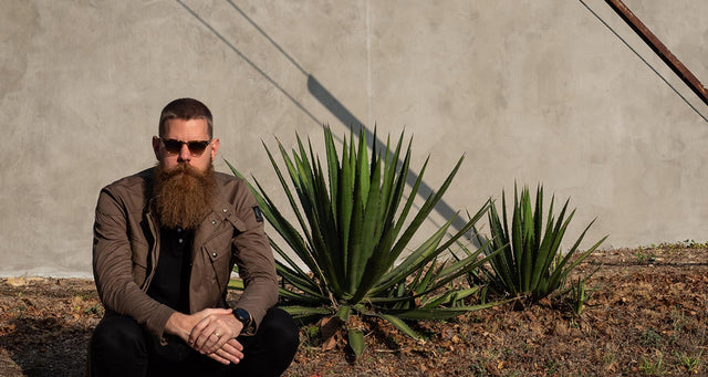 Eric Bandholz has a buzz cut and long beard, and is squatting in front of a cement wall.
