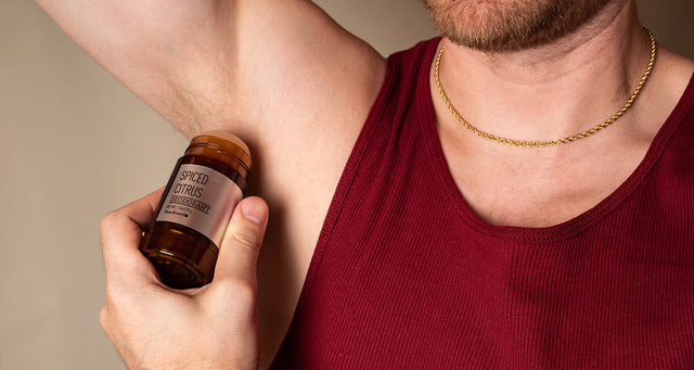 White man in a red tank top applying Beardbrand Deodorant to his armpit.