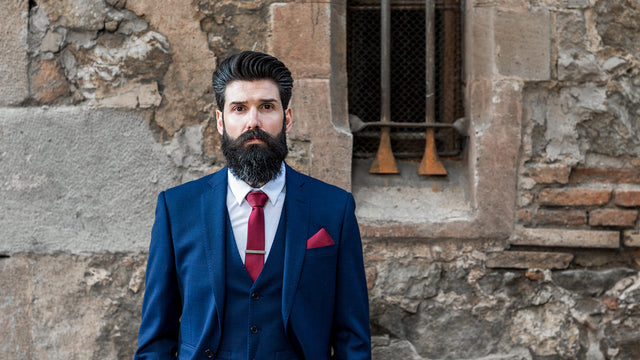 Carlos Costa has an amazing beard style and is wearing a blue 3-piece suit and red tie. 