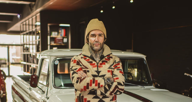 Carlos Costa with mutton chops standing in front of a classic car. 