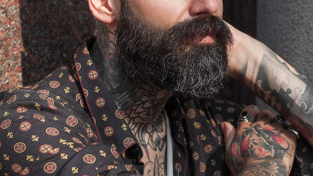Close up of a man's thick, black beard and visible neck tattoos. 