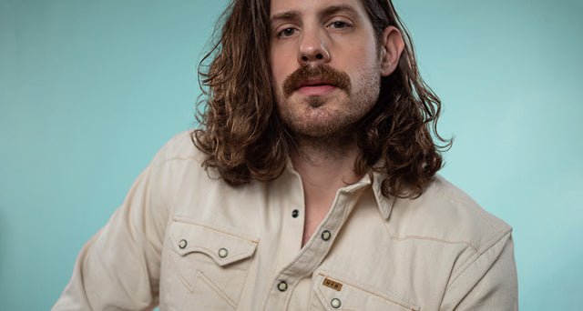 A portrait of Mike against a light teal backdrop wearing a pearl snap shirt.