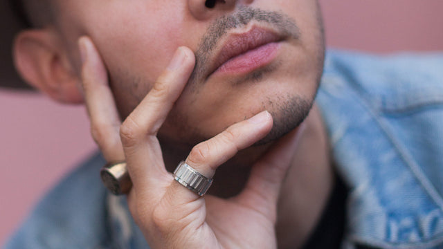 Close up of a man touching his face. He has clear, healthy skin and facial hair stubble. 