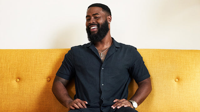 Stylish Black man with a thick beard, smiling and sitting on a yellow couch. 