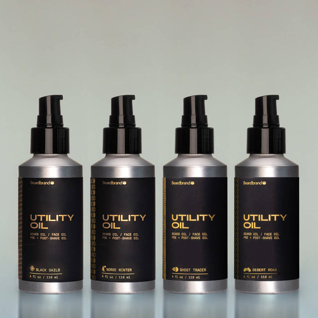 4 bottles of Utility Oil side by side with a pump dispenser against a grey background. From left to right: Black Sails, Norse Winter, Ghost Tracer and Desert Road.