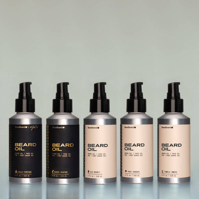 Five bottles of full-size Beard Oil (Bold Fortune, Norse Winter, Old Money, Tree Ranger and Temple Smoke) side by side against a grey background.