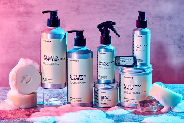 Beardbrand grooming products displayed with accents foam and a clear prisms, under pink, blue and purple hues.