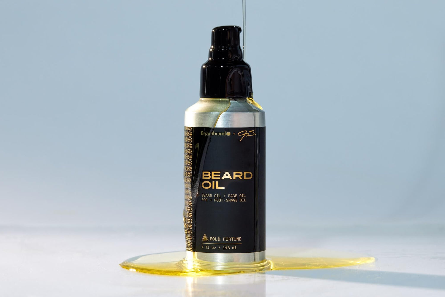 Beardbrand Bold Fortune Beard Oil bottle with oil pooled at the base on a light blue background.