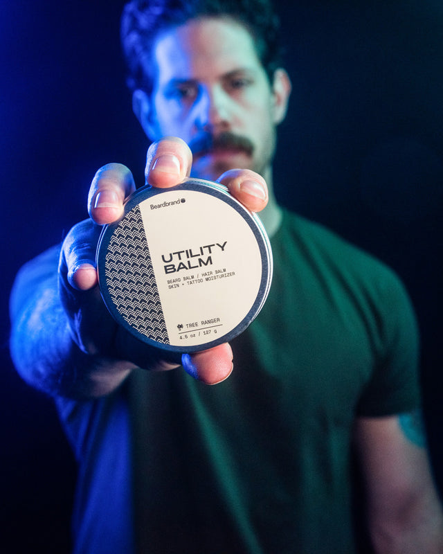 Mike holding a canister of Beardbrand Utility Balm out facing forward to show the top lid label.