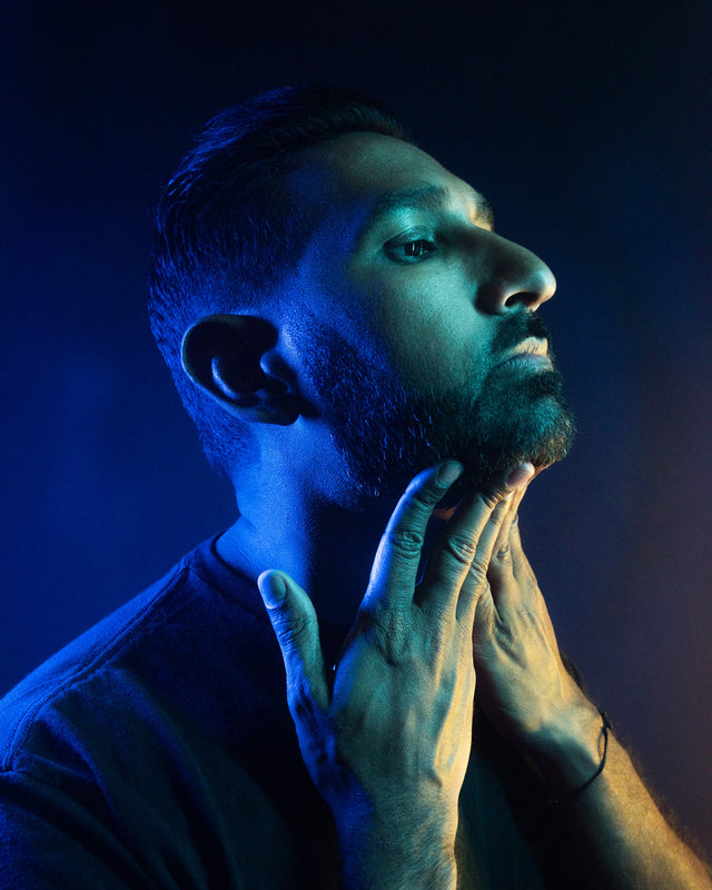Side profile of a beardsman in vibrant lighting while applying product to their beard.
