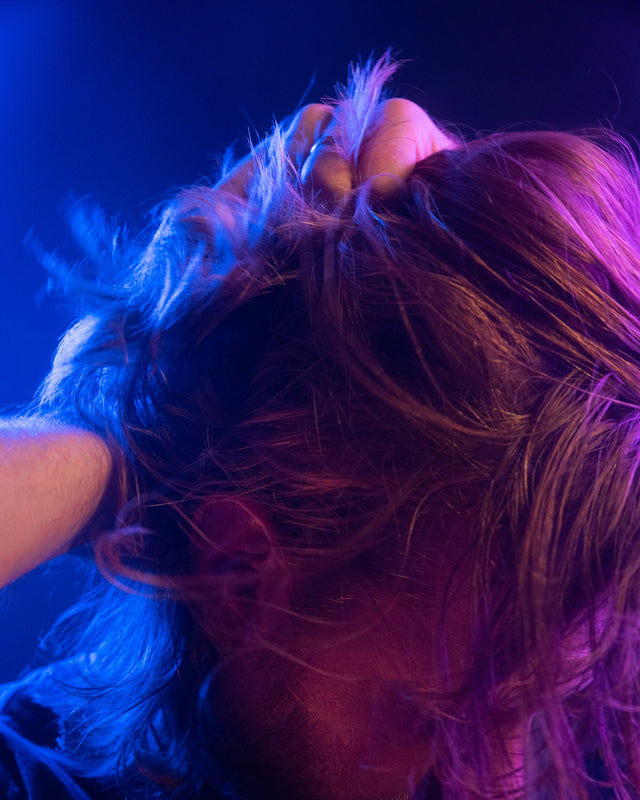 A person running their hands through their long hair in vibrant lighting.