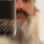 Bearded man applying Beardbrand Four Vices Cologne rollerball to his neck and showing the bottle.