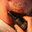 Close-up of stubbled lower face with Beardbrand Four Vices Eau de Parfum roll-on bottle held against the skin.