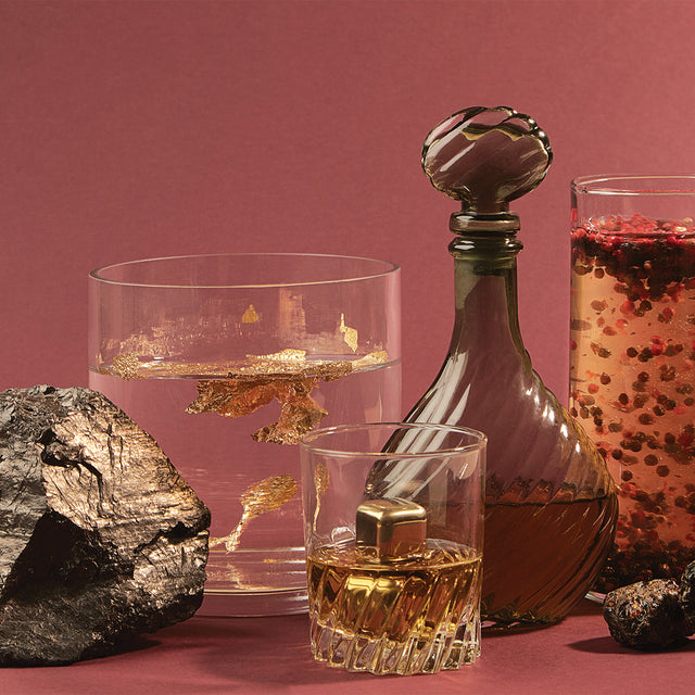 A still life of items reminiscent of Old Money's fragrance notes: glasses of various liquids with gold flakes and cubes hovering inside.