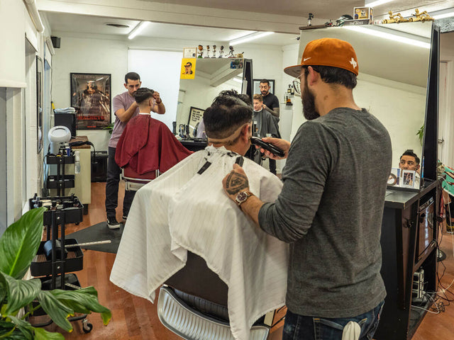 A busy barbershop scene with multiple barbers giving haircuts, showcasing modern grooming and community atmosphere.