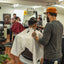 A busy barbershop scene with multiple barbers giving haircuts, showcasing modern grooming and community atmosphere.