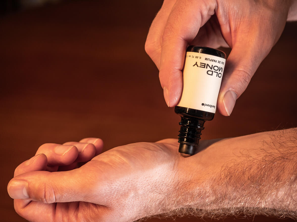 Man applying Beardbrand Old Money Beard Oil onto his wrist before grooming, highlighting premium men’s fragrance and beard care.
