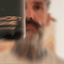 Bearded man applying Beardbrand Short Game Cologne rollerball to his neck and showing the bottle.