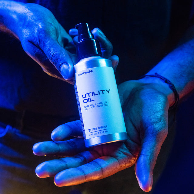 A person showing in their hands the front of Beardbrand Utility Oil in vibrant lighting.