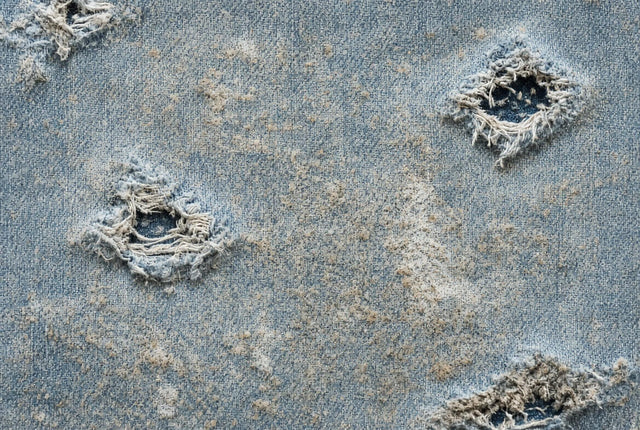 Close-up of faded blue denim fabric with frayed holes, distressed details, and a worn, vintage texture.