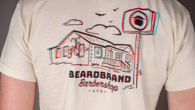 A person displaying the back graphic of the Beardbrand Barbershop 3D tee, featuring the exterior design of Beardbrand Barbershop.