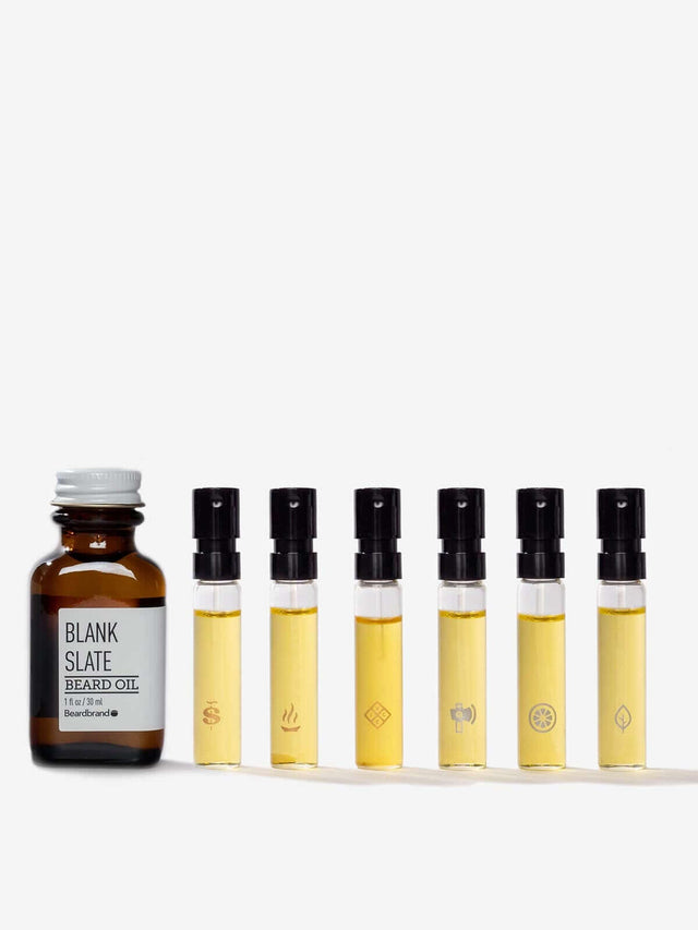 A bottle of Beardbrand Blank Slate Beard Oil next to six vials of Beardbrand Gold & Silver Line Fragrance Samples—Old Money, Temple Smoke, Four Vices, Tree Ranger, Spiced Citrus, and Tea Tree.